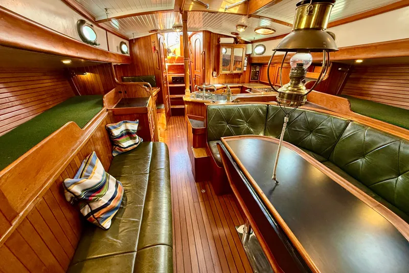 Slide: The Image of Interior of a 1977 Hans Christian Ketch sailboat with wood paneling and green leather seating. - 24