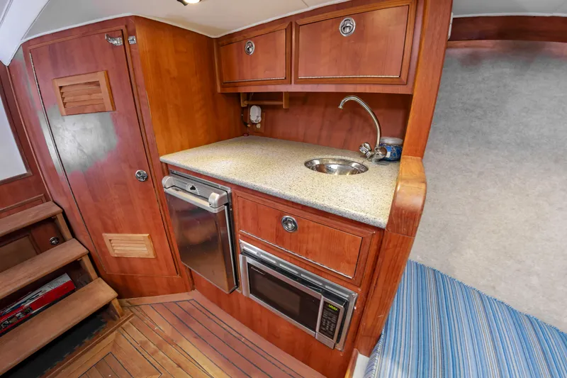Slide: The Image of The 2006 Custom Carolina 36 Express galley features wooden cabinets, a sink, and a microwave. - 33