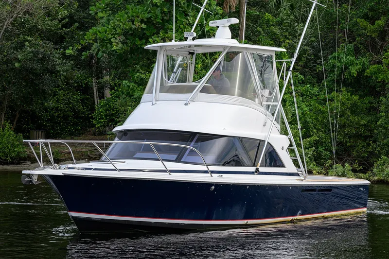 Slide: The Image of 2018 Bertram 35 Flybridge boat cruising on a calm river, surrounded by lush greenery. - 3