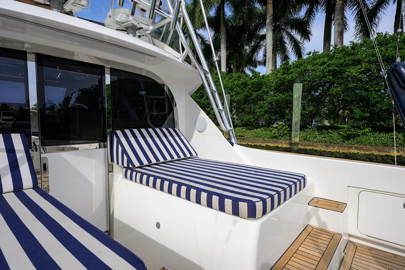 Slide: The Image of 2018 Bertram 35 Flybridge with striped cushions, docked near lush greenery. - 21