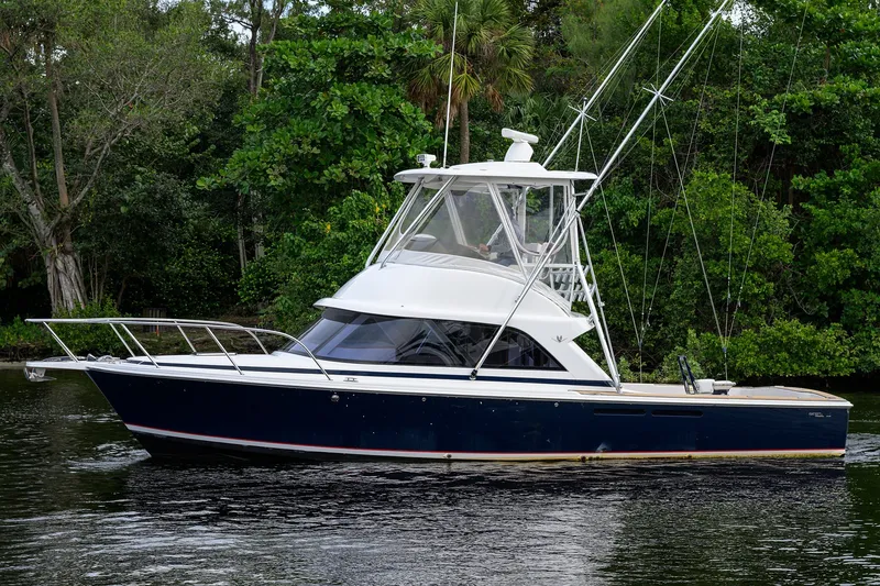 Slide: The Image of 2018 Bertram 35 Flybridge boat on calm water, surrounded by lush greenery. - 10