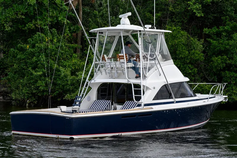 Slide: The Image of 2018 Bertram 35 Flybridge yacht cruising on a serene waterway, surrounded by lush greenery. - 1