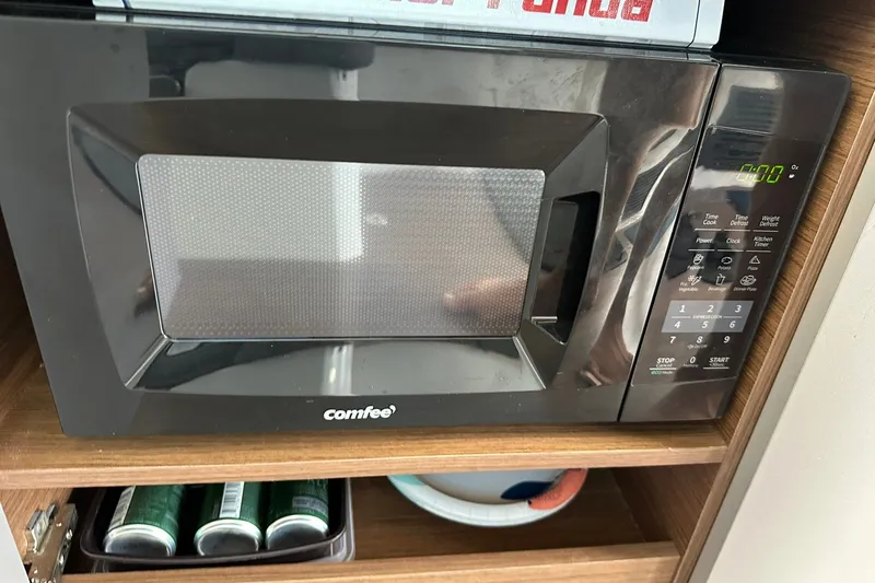 Slide: The Image of Microwave oven in a Beneteau Antares 11 Fly 2024, with digital controls and wooden shelving. - 62