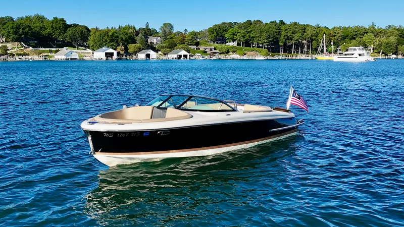 Slide: The Image of A 2016 Chris-Craft Carina 21 floats on calm water. The setting is wooded with some buildings onshore. - 13
