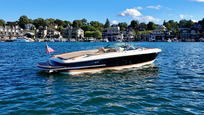 Slide: The Image of A sleek 2016 Chris-Craft Carina 21 boat on calm water, with a scenic coastal town backdrop. - 39