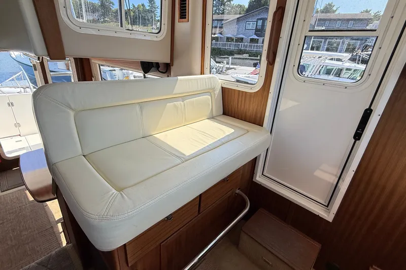 Slide: The Image of Cozy interior seating on a 2012 American Tug 365 boat, featuring white upholstery and wooden accents. - 100