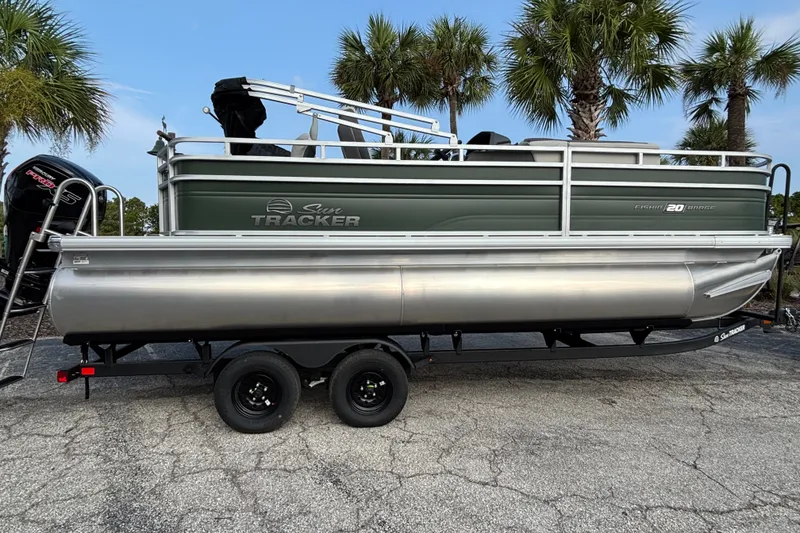 The Image of 2027 Sun Tracker Fishin' Barge 20 DLX pontoon boat on trailer, surrounded by palm trees. - 0