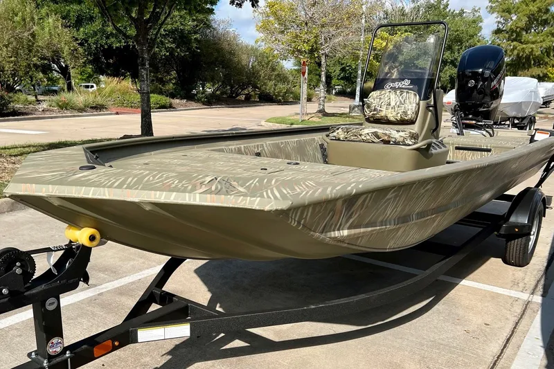 The Image of 2027 Tracker Grizzly 1860 CC boat on trailer, featuring camouflage design and outboard motor. - 0