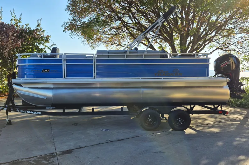 The Image of 2027 Sun Tracker SportFish 20 DLX pontoon boat on trailer, parked outdoors. - 0