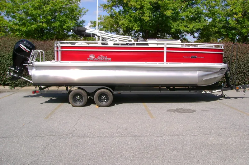 The Image of 2027 Sun Tracker Fishin' Barge 22 DLX pontoon boat on trailer, parked outdoors. - 0