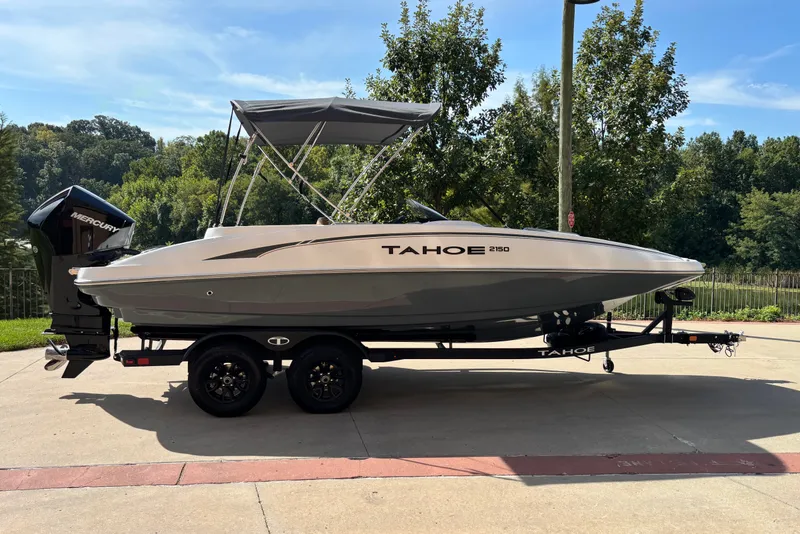 The Image of 2027 Tahoe 2150 boat on trailer, parked outdoors with trees in the background. - 0