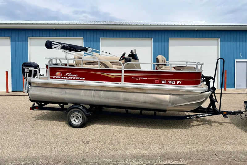 The Image of 2022 Sun Tracker Bass Buggy 18 DLX pontoon boat on trailer, parked near blue building. - 0