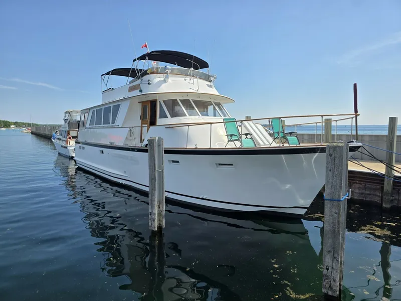 The Image of A 1976 Chris-Craft Roamer 60 docked at a calm pier, with blue chairs on the deck. - 1