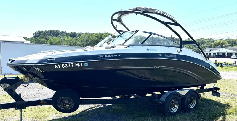 The Image of A 2013 Yamaha 242 Limited S boat on a trailer, featuring sleek design and a Bimini top. - 1