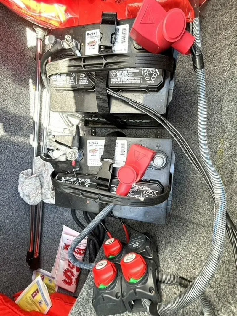 Slide: The Image of Batteries and wiring in a boat, featuring red covers and gray carpeted flooring. - 36