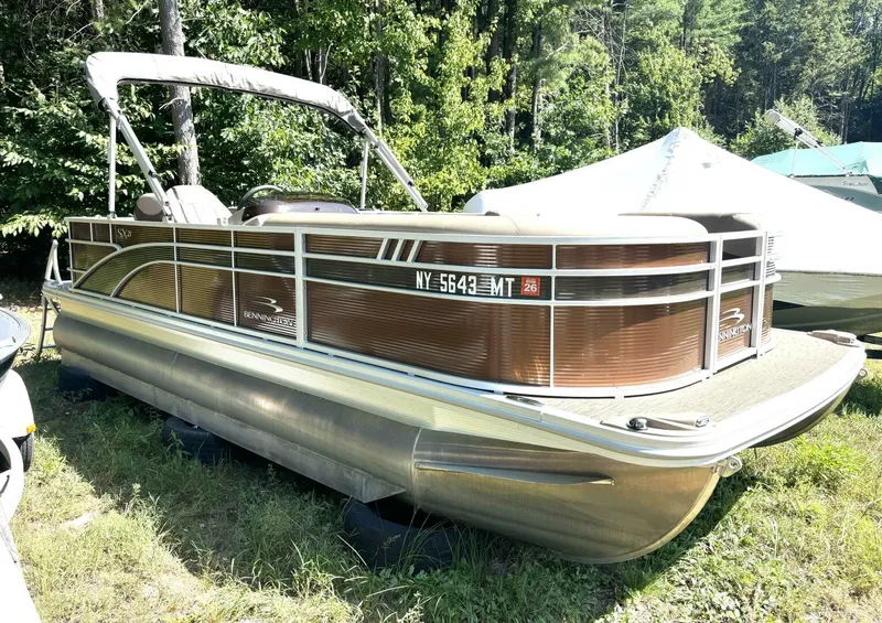 Slide: The Image of A 2023 Bennington 21 SXSAPG pontoon boat is on a grassy area, surrounded by trees. - 3