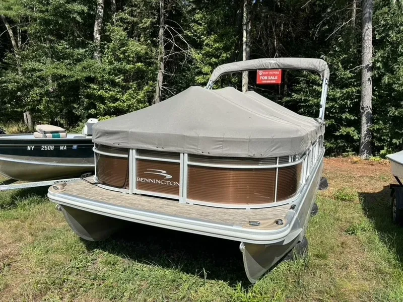 Slide: The Image of 2023 Bennington 21 SXSAPG pontoon boat with gray cover, parked on grass, surrounded by trees. - 36