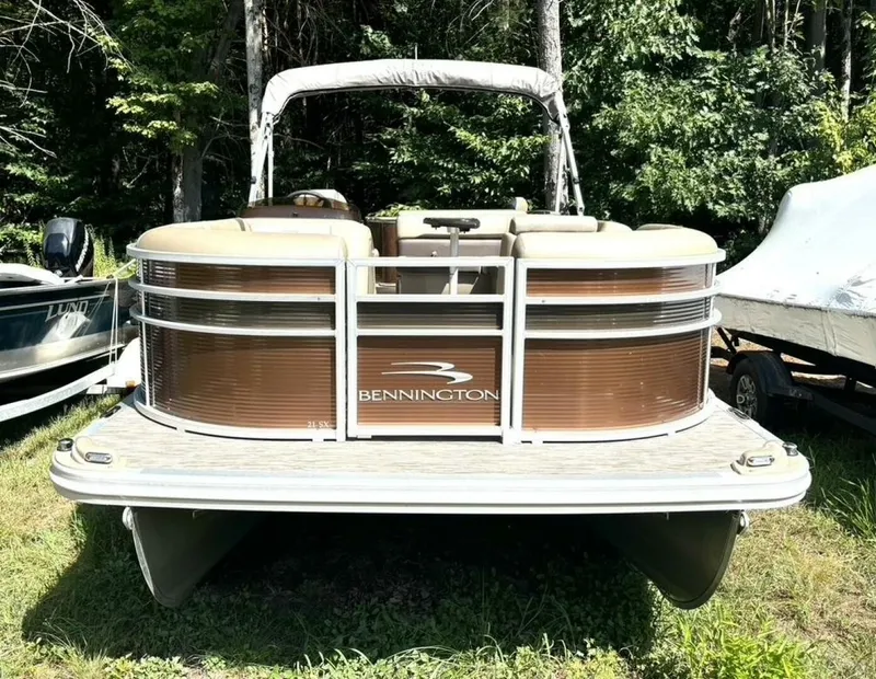 Slide: The Image of A 2023 Bennington 21 SXSAPG pontoon boat is on grass, surrounded by trees. - 2