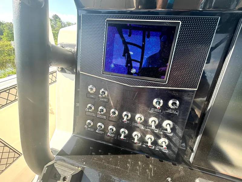 Slide: The Image of The image shows the dashboard of a 2019 Wellcraft 302 Center Console boat with multiple switches and a screen. - 24