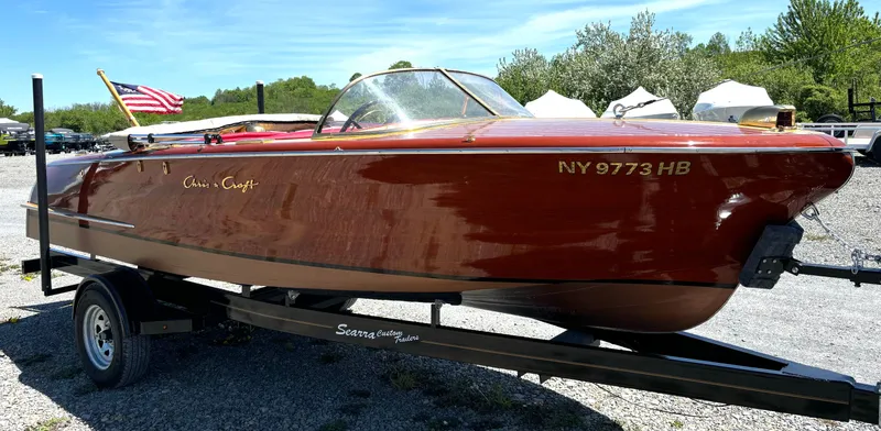 The Image of A classic 1956 Chris-Craft Capri boat on a trailer, featuring an American flag. - 1