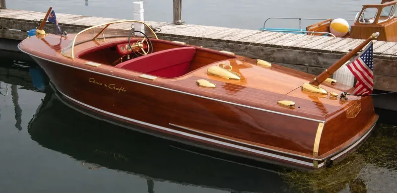 Slide: The Image of A classic 1956 Chris-Craft Capri boat with polished wood and red seats at the dock. - 38