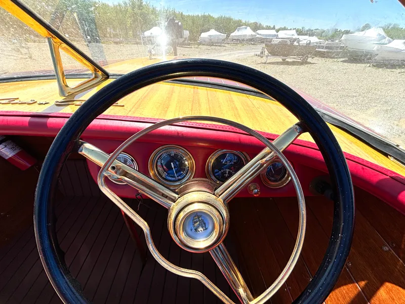 Slide: The Image of 1956 Chris-Craft Capri with classic wooden steering wheel and dashboard, surrounded by other boats outdoors. - 21