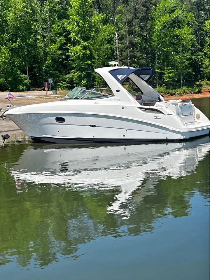 The Image of A white 2010 Sea Ray Sundancer 310 boat sits calmly on a lake, surrounded by trees. - 1