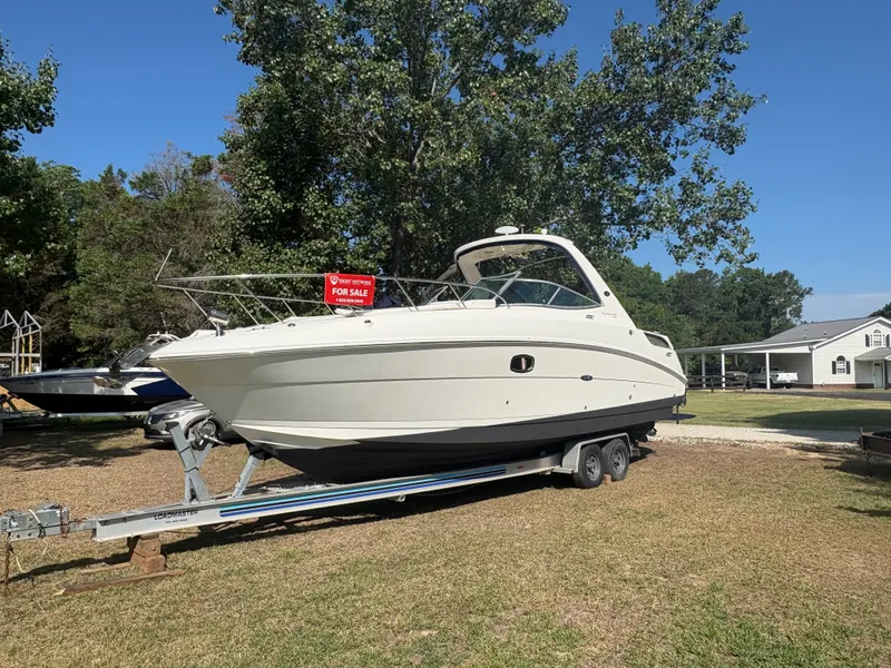 Slide: The Image of A 2010 Sea Ray Sundancer 310 is on a trailer outdoors, with a for sale sign. - 2