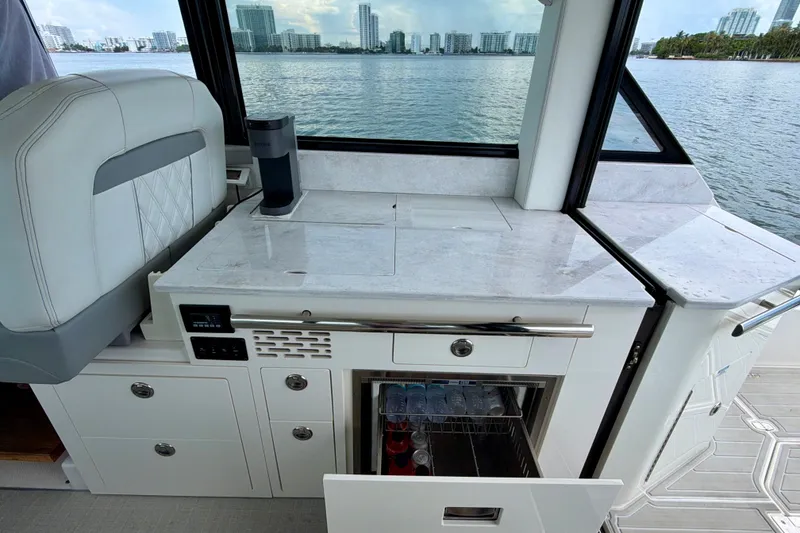 Slide: The Image of 2022 Regal 36 XO yacht interior with kitchenette and beverage storage, overlooking waterfront cityscape. - 24
