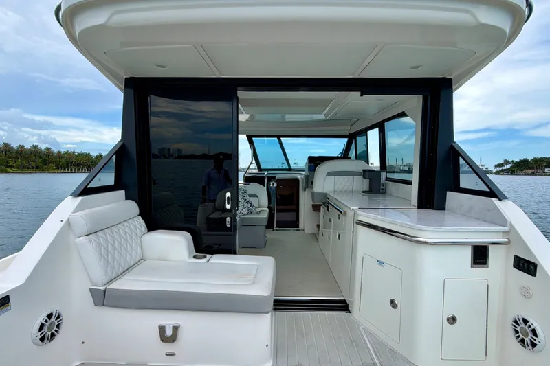 Slide: The Image of 2022 Regal 36 XO yacht interior with seating and kitchenette, docked by scenic waterfront. - 13