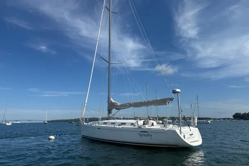 Slide: The Image of 2006 Beneteau First 44.7 sailboat anchored in a serene harbor under a clear blue sky. - 2