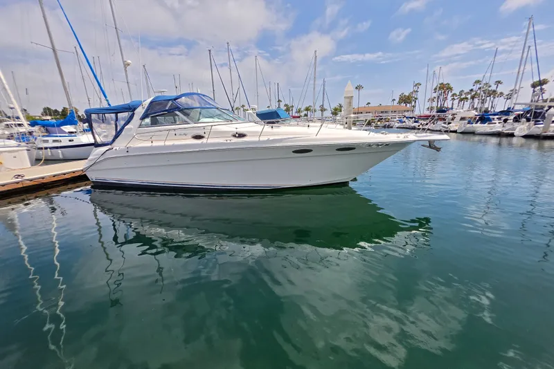 The Image of A 1999 Sea Ray Sundancer 330 docked in a marina. It features a white hull and blue canopy. - 0