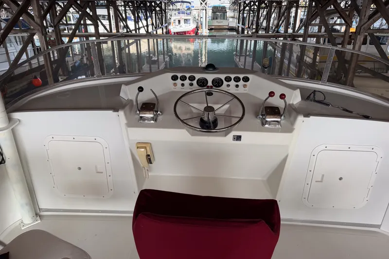 Slide: The Image of 1990 Cruise-A-Home Corsair boat helm with steering wheel and control panel in marina setting. - 14