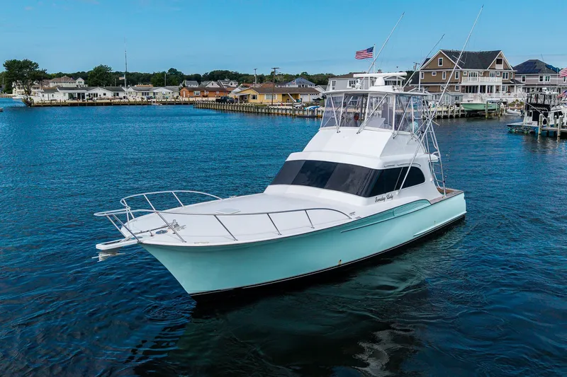 Slide: The Image of 1986 Buddy Davis 47 Convertible yacht on calm waters near a coastal town. - 55
