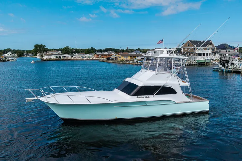 Slide: The Image of 1986 Buddy Davis 47 Convertible yacht on serene water with coastal houses in the background. - 4