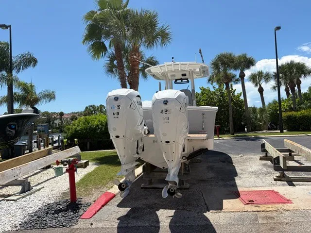 Slide: The Image of A 2022 Regulator 31 boat with twin outboard engines on a trailer, surrounded by palm trees. - 1