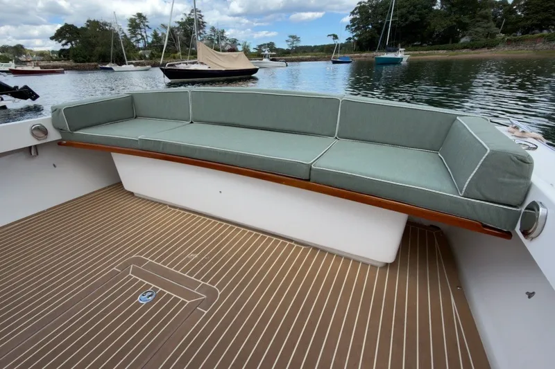 Slide: The Image of Fortier 33 boat with cushioned seating, wooden deck, and scenic waterfront view, 2023 model. - 13