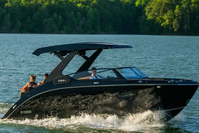 Slide: The Image of 2027 Yamaha Boats 295XD cruising on a scenic lake with lush green forest backdrop. - 2