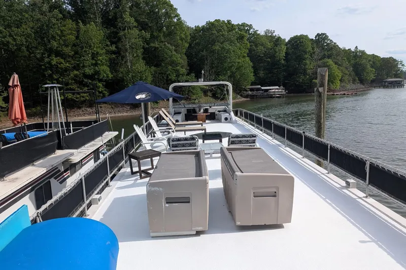 Slide: The Image of 1996 Stardust Cruisers houseboat with spacious deck, lounge chairs, and umbrella on a serene lake. - 36