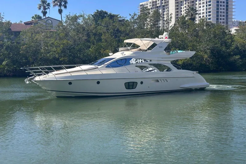 Slide: The Image of 2007 Azimut 55E yacht cruising on a calm river with lush greenery and buildings in the background. - 2