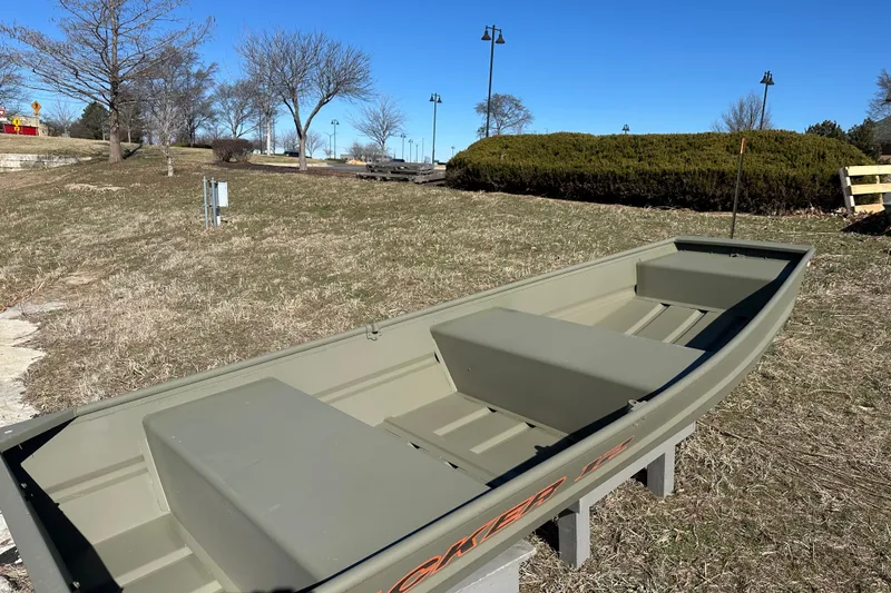 The Image of 2027 Tracker Grizzly 12 Jon boat on grassy landscape under clear blue sky. - 0
