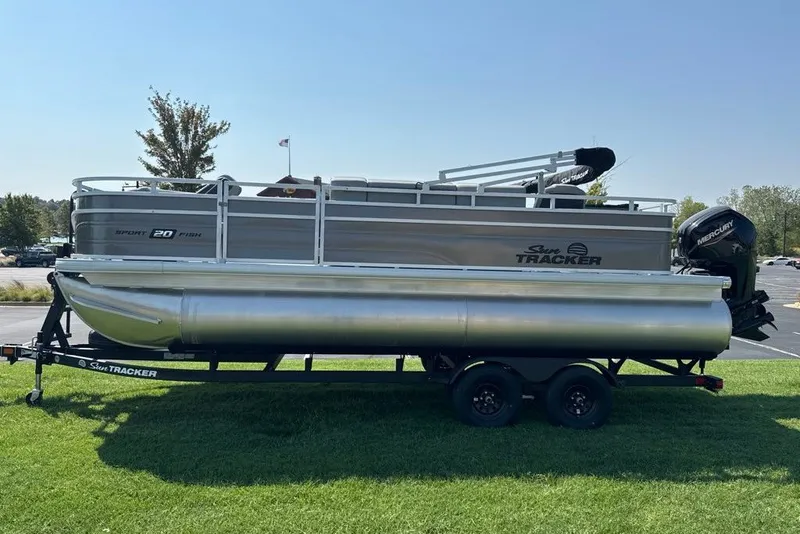 The Image of 2027 Sun Tracker SportFish 20 DLX pontoon boat on trailer, parked on grass. - 0