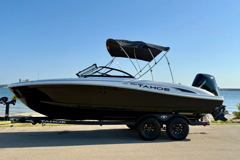 Slide: The Image of 2027 Tahoe 210 S boat on trailer by the water, under clear blue sky. - 14