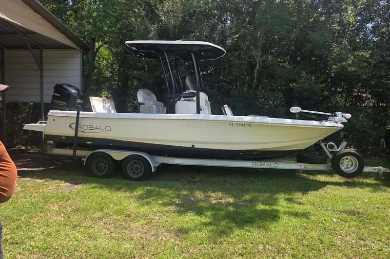 The Image of 2019 Robalo 226 Cayman boat on trailer, parked on grass near trees. - 0