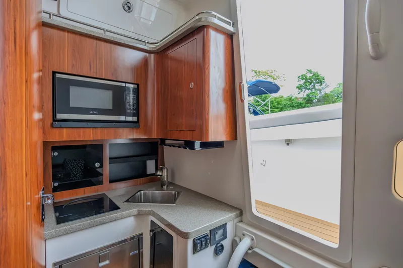 Slide: The Image of 2018 Regulator 41 boat interior with kitchenette, featuring microwave, sink, and wooden cabinetry. - 14