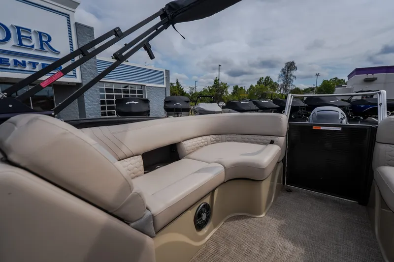 Slide: The Image of 2023 Crest Caribbean LX 250 pontoon boat interior with beige seating and outdoor dealership view. - 28