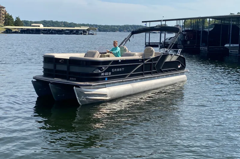 Slide: The Image of 2023 Crest Caribbean LX 250 pontoon boat on a lake, with a person at the helm. - 59