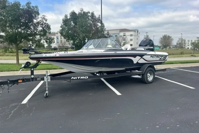 Slide: The Image of 2021 Nitro Z19 boat on trailer in parking lot, surrounded by trees and buildings. - 2