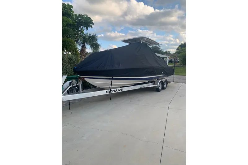 Slide: The Image of 2020 Caymas 26 HB boat covered on trailer, parked on driveway under cloudy sky. - 6