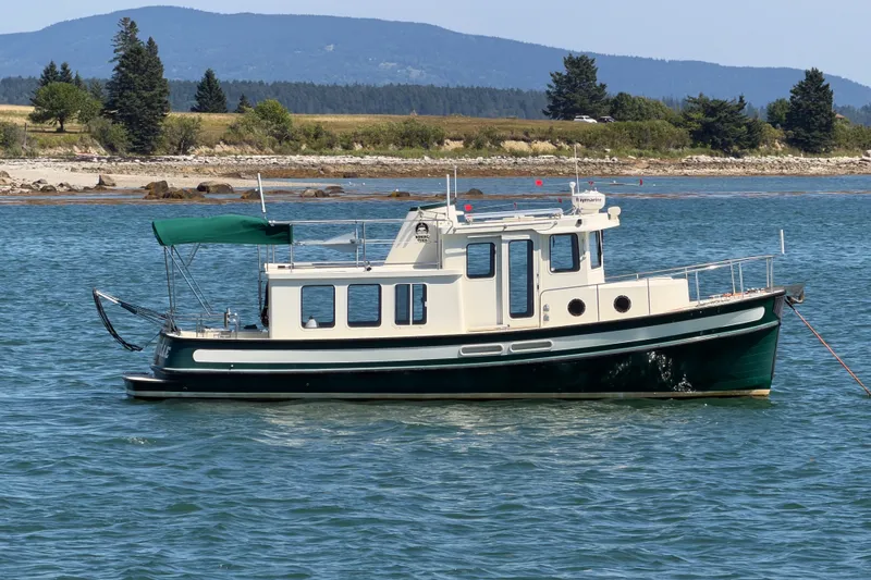 Slide: The Image of 2001 Nordic Tug 32 boat anchored on calm water with scenic background. - 0